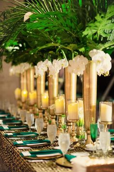 a table topped with lots of gold vases filled with white flowers and greenery