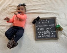 a baby laying on top of a bed next to a sign