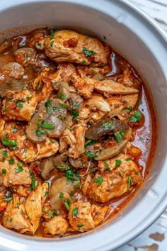 a white bowl filled with chicken and vegetables covered in sauce on top of a table