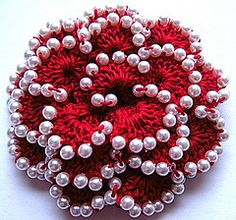 a red and white brooch with pearls on it's center piece, sitting on a white surface