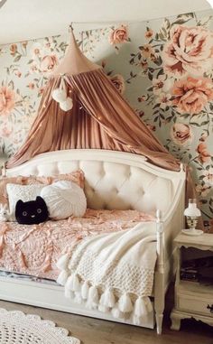 a white bed with pink flowers on the wall and a black cat laying on it