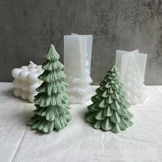 three green christmas trees sitting next to each other on a white cloth covered tablecloth