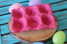 an egg carton made out of foam and eggs on a wooden table with some colored eggs in the background