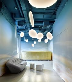 an office with blue walls and ceiling lights hanging from it's ceiling, along with round white stools on the floor