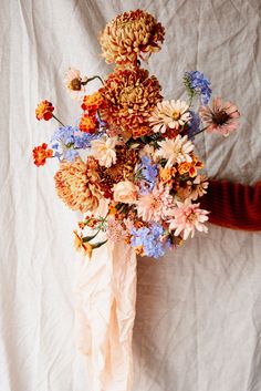 a bouquet of flowers sitting on top of a white cloth covered tablecloth next to a person's arm