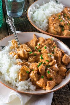 two bowls filled with rice and meat covered in gravy on top of a wooden table