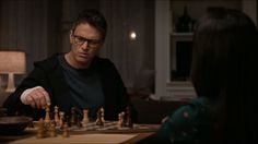 a man sitting at a table with a chess board in front of him and another person looking on