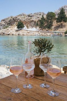 three wine glasses sitting on top of a wooden table next to a body of water