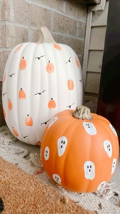 two painted pumpkins sitting next to each other on the floor in front of a fireplace