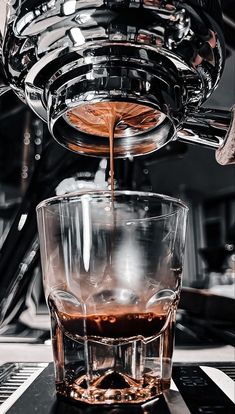 an espresso being poured into a glass on top of a counter with other coffee machines in the background