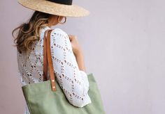 a woman wearing a straw hat and carrying a green tote bag with leather handles