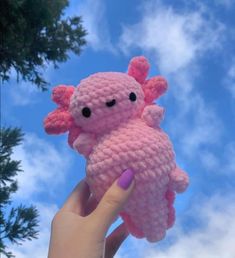 a hand holding a pink crocheted stuffed animal in front of a blue sky