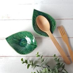 two wooden spoons and a green leaf shaped bowl on a white wood table with greenery