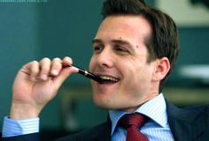 a man wearing a suit and tie is holding a pen to his mouth while smiling