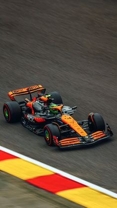 an orange and black race car driving on a track with red, yellow and green stripes