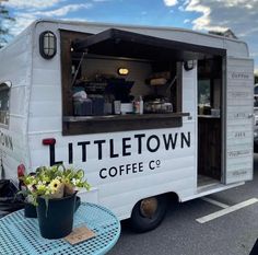 a little town coffee truck parked in a parking lot with flowers and potted plants