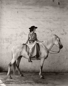 a woman sitting on top of a white horse next to a wall in an old photo