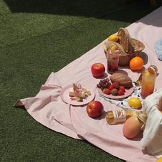 an outdoor picnic with fruit and drinks on the grass in front of a pink blanket