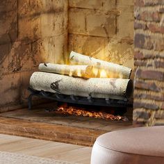 a fireplace with logs burning in it next to a chair and ottoman on the floor