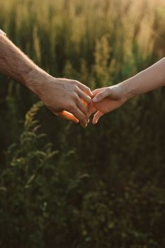 two people holding hands over each other in front of some tall grass and bushes at sunset