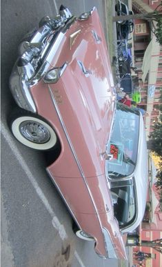 an old pink car parked on the side of the road