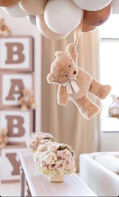 a teddy bear hanging from a bunch of balloons in a baby's room with flowers