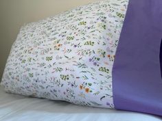 a pillow with flowers on it sitting on top of a white bed sheet and purple sheets