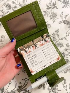 a woman's hand holding a green wallet with a calendar attached to the front