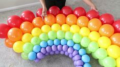 a rainbow made out of balloons on the floor with a woman standing next to it