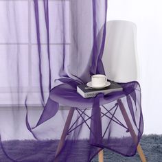 a chair with a book and cup on it in front of a sheer purple curtain