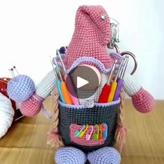 a crocheted stuffed animal holding a basket filled with pens, scissors and pencils