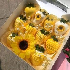 a box filled with yellow and white chocolates covered in sunflowers next to flowers