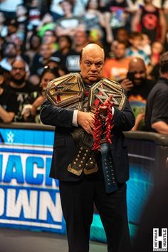 a man in a suit and wrestling belt standing on a stage with his arms crossed