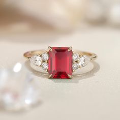 a close up of a ring with a red stone in the middle and two diamonds around it