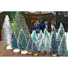 christmas trees are lined up on a table in front of a vase and other decorations