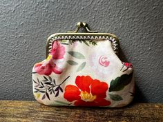 a small purse sitting on top of a wooden table next to a gray wall with flowers