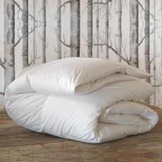 an unmade bed with white comforter and pillows on the floor in front of wallpaper