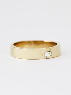 a yellow gold wedding band with a baguette cut diamond in the center, on a white background