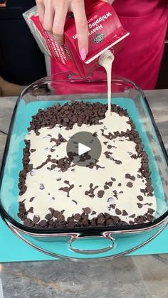 a person pouring chocolate chips into a cake with white frosting on top and an ipod in the middle