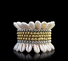 A Handmade Tribal Traditional New Guinea braided rope wide bracelet, decorated with two bands of cream Cowrie Shells, two bands of silver round beads, and three central bands of golden beads. The inner diameter of the bracelet is 2 inches (expands), and the maximum height of the bracelet is 2- 3/8 inches. The total length of the opened, flattened band of the bracelet is 6- 2/8 inches. The bracelet is finished, at each end, with two, approximately 5 inches cords (for adjustable sizing), each deco White Beaded Bohemian Cuff Bracelet, Adjustable White Bohemian Cuff Bracelet, Bohemian White Cuff Bracelet With Round Beads, Handmade White Cuff Bracelet For Festival, Bohemian Cream Bangle Jewelry, Bohemian Cream Bangle, White Bohemian Stretch Bracelet For Festivals, Handmade Bohemian White Stretch Bracelet, Bohemian Cream Stretch Bracelet As Gift