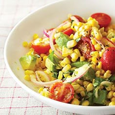 a white bowl filled with corn, tomatoes and avocado on top of a table