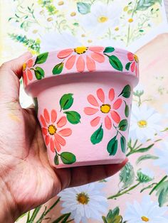 a hand holding a pink flower pot with flowers on it