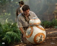 a man kneeling down next to a star wars bbg ball in the woods with other people behind him