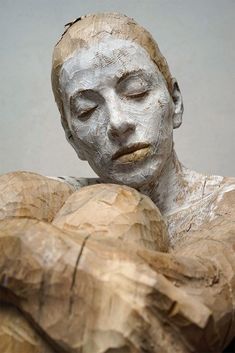 a sculpture of a woman with her eyes closed and hands folded over her head, holding a rock