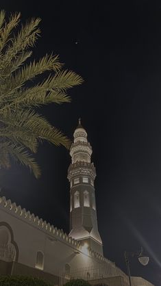 a tall white tower with a clock on it's side next to a palm tree