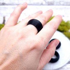 a person's hand with a black ring on their finger and moss growing in the background