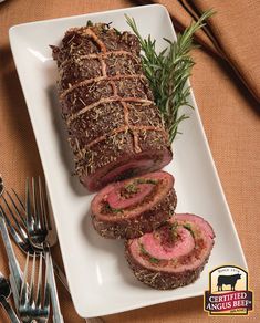 a white plate topped with sliced meat next to utensils