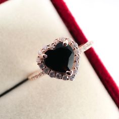 a heart shaped black diamond ring sitting on top of a red velvet cushioned box