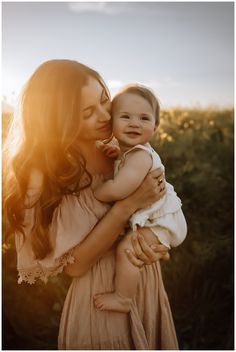 a woman holding a baby in her arms and smiling at the camera with sun shining on her