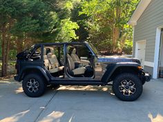 a black jeep parked in front of a house with its door open and the driver's seat up